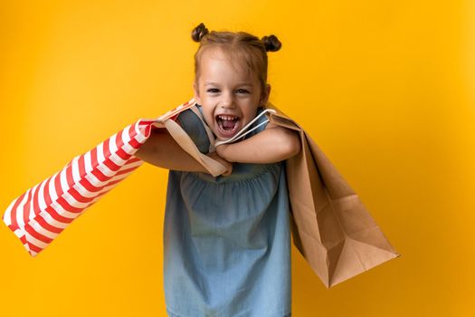 Portrait Caucasian Beautiful Happy Little Preschool Girl Smiling Cheerful And Holding Heavy Cardboard Bags Isolated On Orange Yellow Background. Happiness, Consumerism, Sale People shopping Concept.