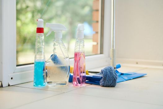 Cleaning products, household chemicals, detergents, rags and mop on the floor against panoramic window background. Housekeeping, chores, spring cleaning, cleaning service concept. Copy ad space