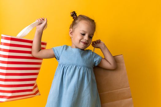 Portrait Caucasian Beautiful Happy Little Preschool Girl Smiling Cheerful And Holding Cardboard Bags Isolated On Orange Yellow Studio background. Happiness, Consumerism, Sale People shopping Concept.