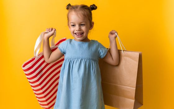 Portrait Caucasian Beautiful Happy Little Preschool Girl Smiling Cheerful And Holding Cardboard Bags Isolated On Orange Yellow Studio background. Happiness, Consumerism, Sale People shopping Concept.