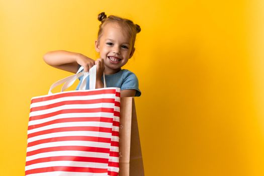 Portrait Caucasian Beautiful Happy Little Preschool Girl Smiling Cheerful And Holding Cardboard Bags Isolated On Orange Yellow Studio background. Happiness, Consumerism, Sale People shopping Concept.