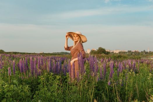 A beautiful woman in a straw hat walks in a field with purple flowers. A walk in nature in the lupin field.