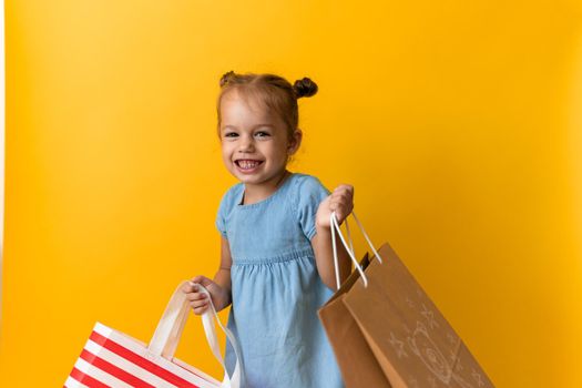 Portrait Caucasian Beautiful Happy Little Preschool Girl Smiling Cheerful And Holding Cardboard Bags Isolated On Orange Yellow Studio background. Happiness, Consumerism, Sale People shopping Concept