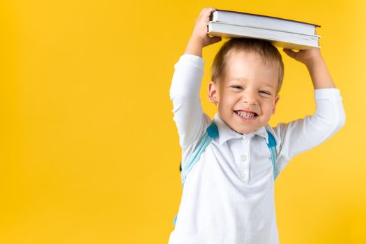 Banner Funny Preschool Child Boy 3-4 years with Book on Head and Bag on Yellow Background Copy Space. Happy Smiling Kid Go Back to School, Kindergarten. Success, Motivation, Genius, Superhero concept.