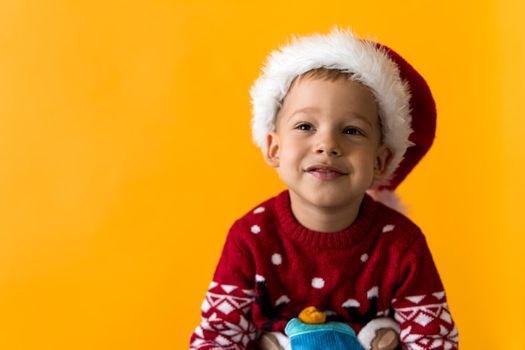 Portrait of happy smiling positive joyful positive preschool little boy in red warm santa hat showing thumb up on orange, yellow background. Winter, holiday, celebration, Christmas, New Year copy space.