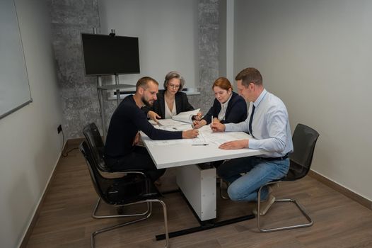 Four colleagues are discussing blueprints in a conference room in an office. Brainstorming of engineers and architects