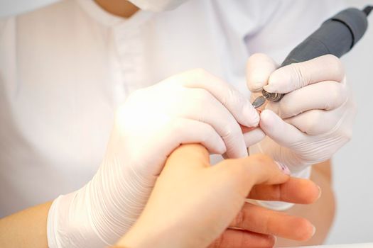Closeup of manicure master removes nail polish uses an electric nail file in a nail salon