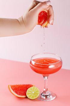 A woman's hand squeezes a grapefruit and drops of juice fall into a glass.