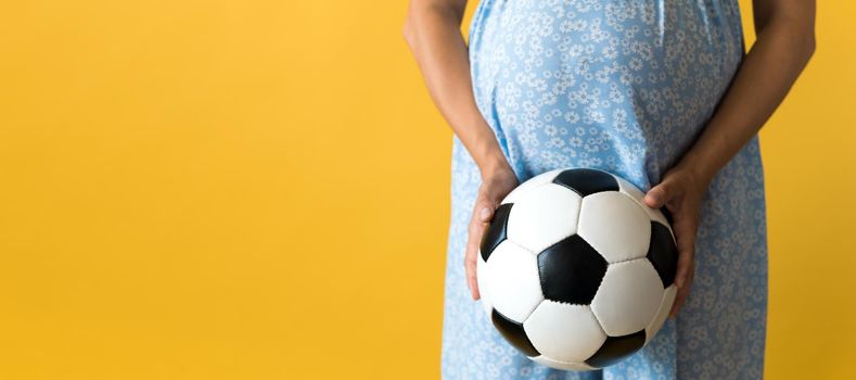 Motherhood, femininity, football, sport, dairy, hot summer. banner pregnant young pretty woman in floral blue dress holds soccer white and black leather classic ball rubs tummy on yellow background.