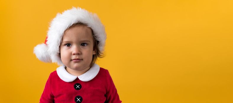 Banner Portraite Cute Happy Cheerful Chubby Baby Girl in Santa Suit Looking On Camera At Yellow Background. Child Play Christmas Scene Celebrating Birthday. Kid Have Fun Spend New Year Time Copy Space.