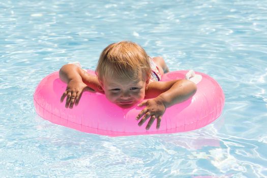 A small child swims in a pink swimming circle in the pool close up