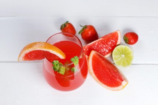 Fresh grapefruit juice in a glass with grapefruit pieces, lime and mint on a wooden background.