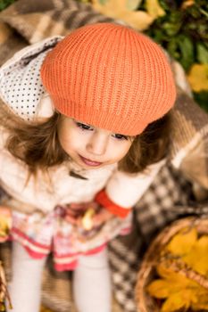 Little Cute Preschool Minor Brunette Girl In Orange Beret Sits On Plaid Covers Dace With Yellow Fallen Maple Leaves In Cold Weather In Fall Park. Childhood, Family, Infant, Motherhood, Autumn Concept