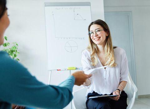 portrait of a smiling young businesswoman doing paperwork and passing document or a contract in the office