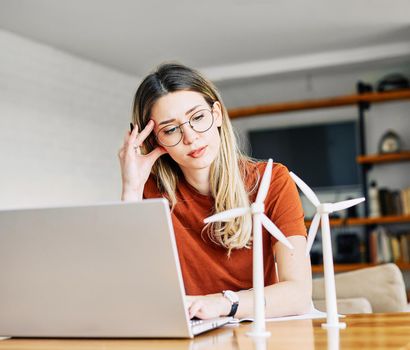 portrait of a young business woman or a student in home office looking at a windmill model and using a laptop computer in the office