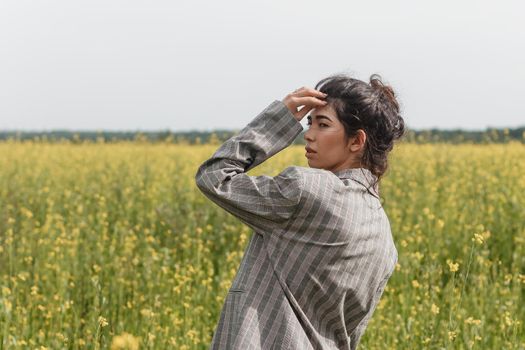 An Asian model poses in a field of yellow flowers for a clothing brand, polyethylene is the main props for a photo shoot. The concept of manufacturing clothing from recycled plastic. A woman in a pantsuit is standing on a plastic bag.