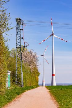 Huge wind turbines and electricity pylons for generating green electricity stand next to a dirt road in rural Germany