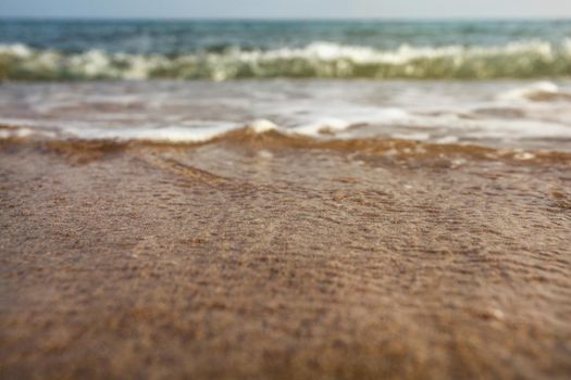 Very low angle (camera on ground, close up) sea water washing the sand. Selective focus on the wet beach, abstract summer holiday / vacation background.