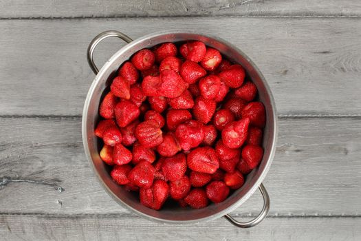 Tabletop view, steel pot full of strawberries with leaves removed. Homemade strawberry jam preparation.