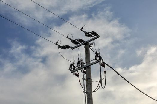 Small concrete pillar with power lines, sky with clouds in background.