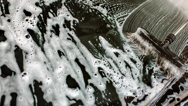 Widshield of a car being washed in self serve carwash, brush leaving strokes in white shampoo and foam on glass.