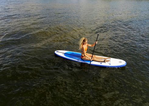 Sup surfing, happy blonde girl with paddle sailing on a board in river. Stand up paddle boarding in summer