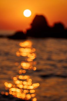 Sunset sky reflecting in the water. Blurry orange and golden skylight calmness relaxing summer mood. Blurred defocused ocean seascape with rocks. Travel destination, vacations concept. .