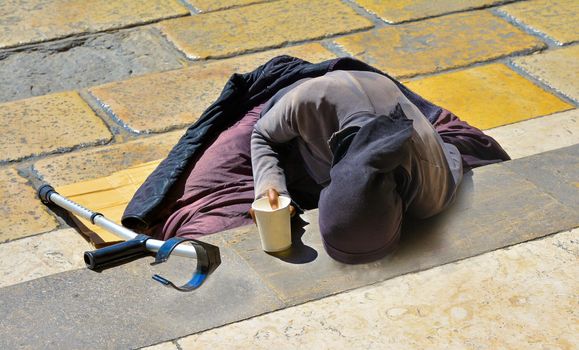 A woman in black clothes with a crutch begging for alms lying on the stairs in Europe