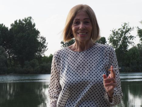 female pensioner having fun and smoking a cigarette in a park - aging free and wellness concept