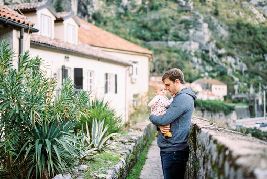 Dad with a baby in his arms stands near a stone fence in front of an old house at the foot of the mountains. High quality photo