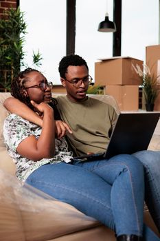 Husband and wife looking at furniture on online website, using laptop to buy things for new beginnings. Enoying relocation and shopping for decorations, moving in apartment flat together.