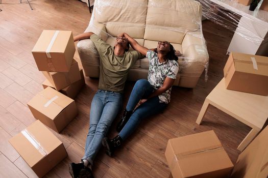 Happy partners taking break after moving in together, enjoying new beginnings in apartment flat. Sitting on living room floor and talking about future family, dreaming about achievement.