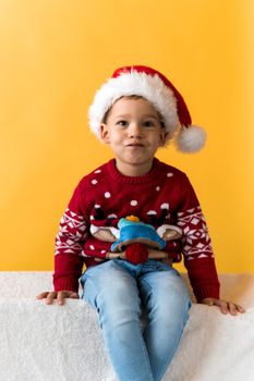 Portrait of happy smiling positive joyful positive preschool little boy in red warm santa hat showing thumb up on orange, yellow background. Winter, holiday, celebration, Christmas, New Year copy space.