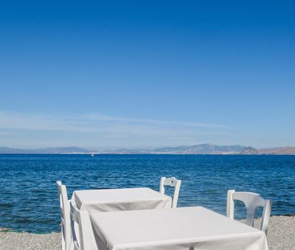 White restaurant tables on the beach in summer - travel, vacation and summer concept. The perfect lunch with a sea view