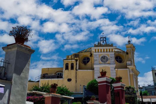 Exterior day view of Roman Catholic church with clock tower Santa Maria delle Grazie in Campania region, Ischia Italy under blue sky with clouds.