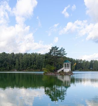 A small beautiful island on Lake Aya in the Altai Territory or the Altai Republic. There is a small gazebo on the island and a forest around the lake.