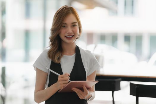 Beautiful Asian women Barista smiling and using tablet at her cafe.