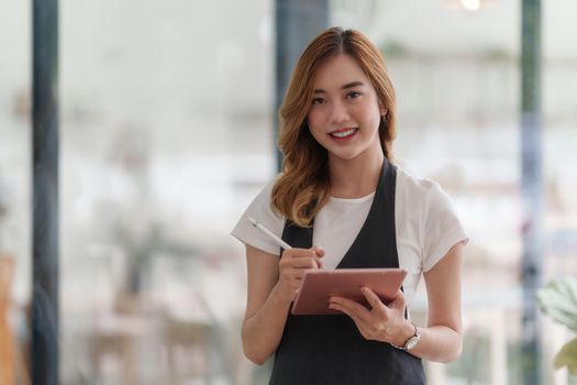 Beautiful Asian women Barista smiling and using tablet at her cafe.