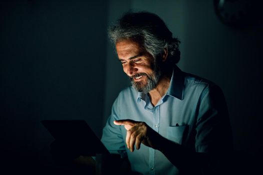 Portrait of a senior businessman with tablet or laptop working late at night in office