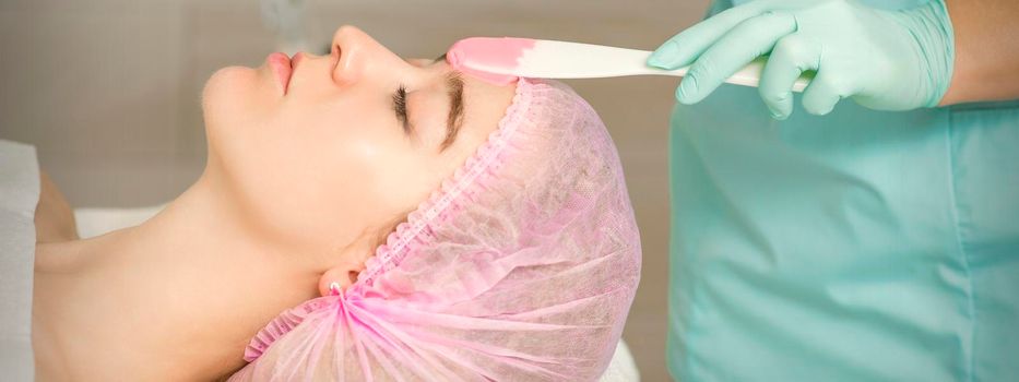 Close up of beautician's hand applying alginate mask on the face of the young caucasian woman in a beauty salon