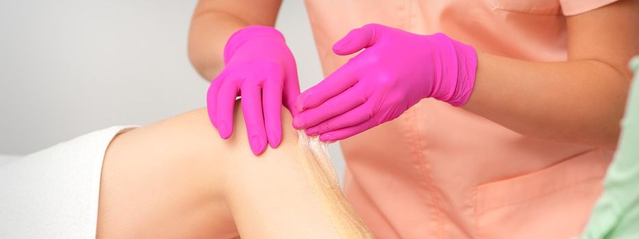 Hands of a beautician in pink gloves epilating leg of a young female in hair removal salon