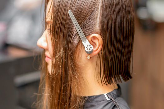 Close up side view of young brunette caucasian woman with split hair in sections in a hair salon