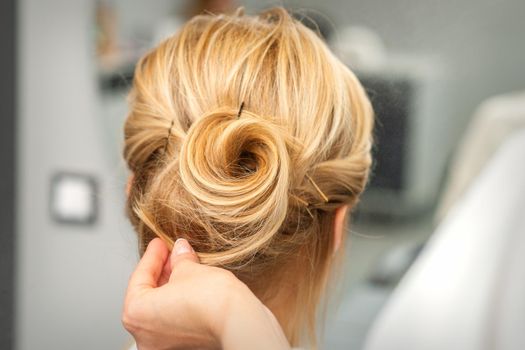 Close up of female hairdresser styling blonde hair of a young woman in a beauty salon
