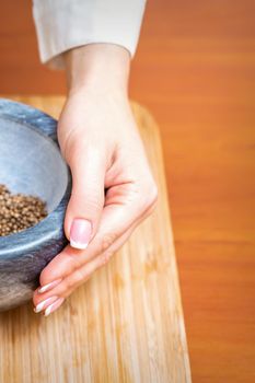 Vertical image of female hand holds mortar with dry pepper spices on a wooden kitchen board