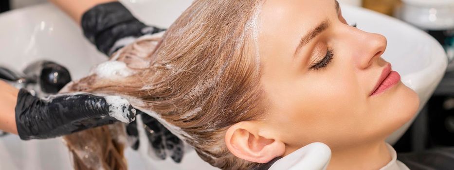 Beautiful young caucasian woman receiving wash her hair in a hair salon