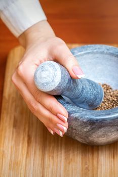 Female hands grind dry pepper spices in mortar on a wooden kitchen board