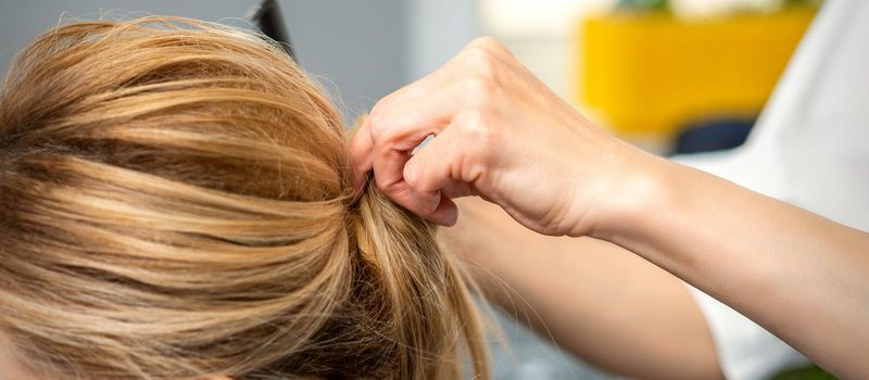 Close up of female hairdresser styling blonde hair of a young woman in a beauty salon