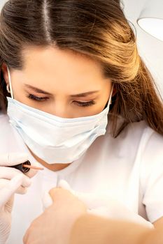 Manicure master in the white protective mask is painting nails with nail polish in a nail salon