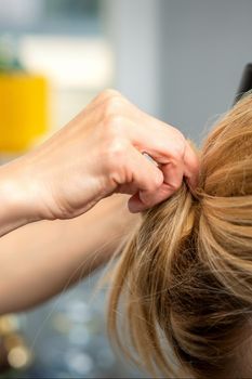 Close up of female hairdresser styling blonde hair of a young woman in a beauty salon