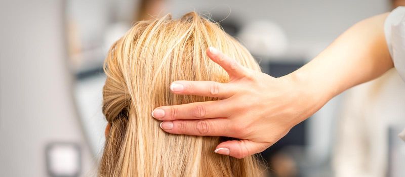 Close up of female hairdresser styling blonde hair of a young woman in a beauty salon